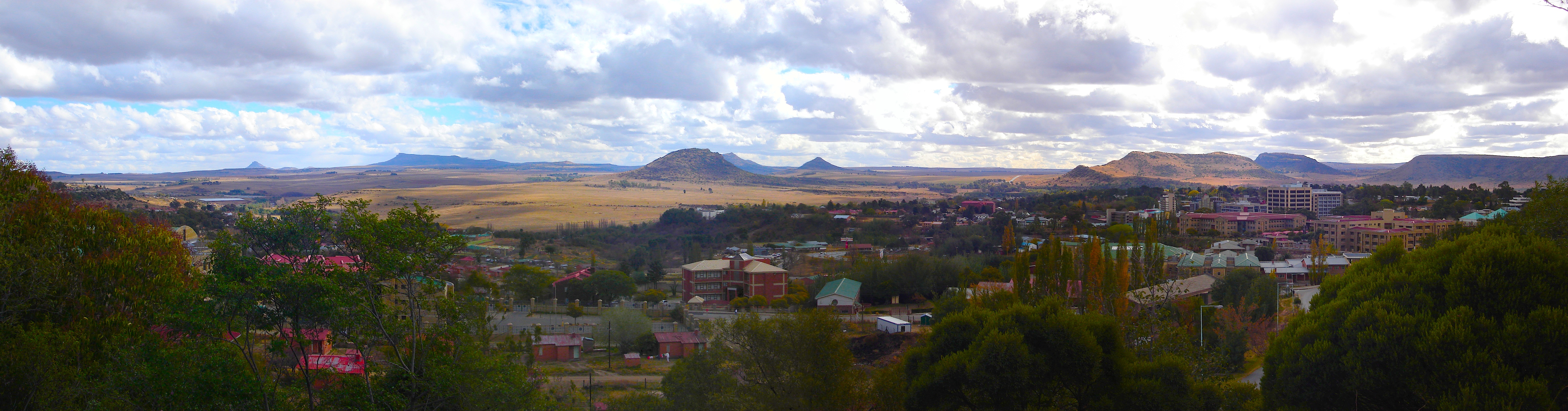 Maseru 2007. Die Landschaft hinter den Gebäuden gehört zu Südafrika. (Panorama-Ansicht durch anklicken; Quelle: Wikipedia, Netroamer (CC BY 3.0))